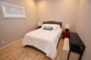 A bedroom with a bed, bedside tables, a lamp, a bench, and a window with blinds. - The Chicken Coop, a Modern Riverfront Oasis (908) (Osceola)