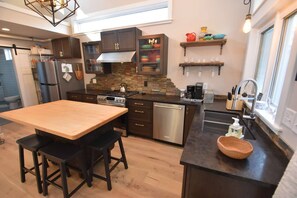A modern kitchen with a central island, dark cabinetry, and a stone backsplash. - The Chicken Coop, a Modern Riverfront Oasis (908) (Osceola)