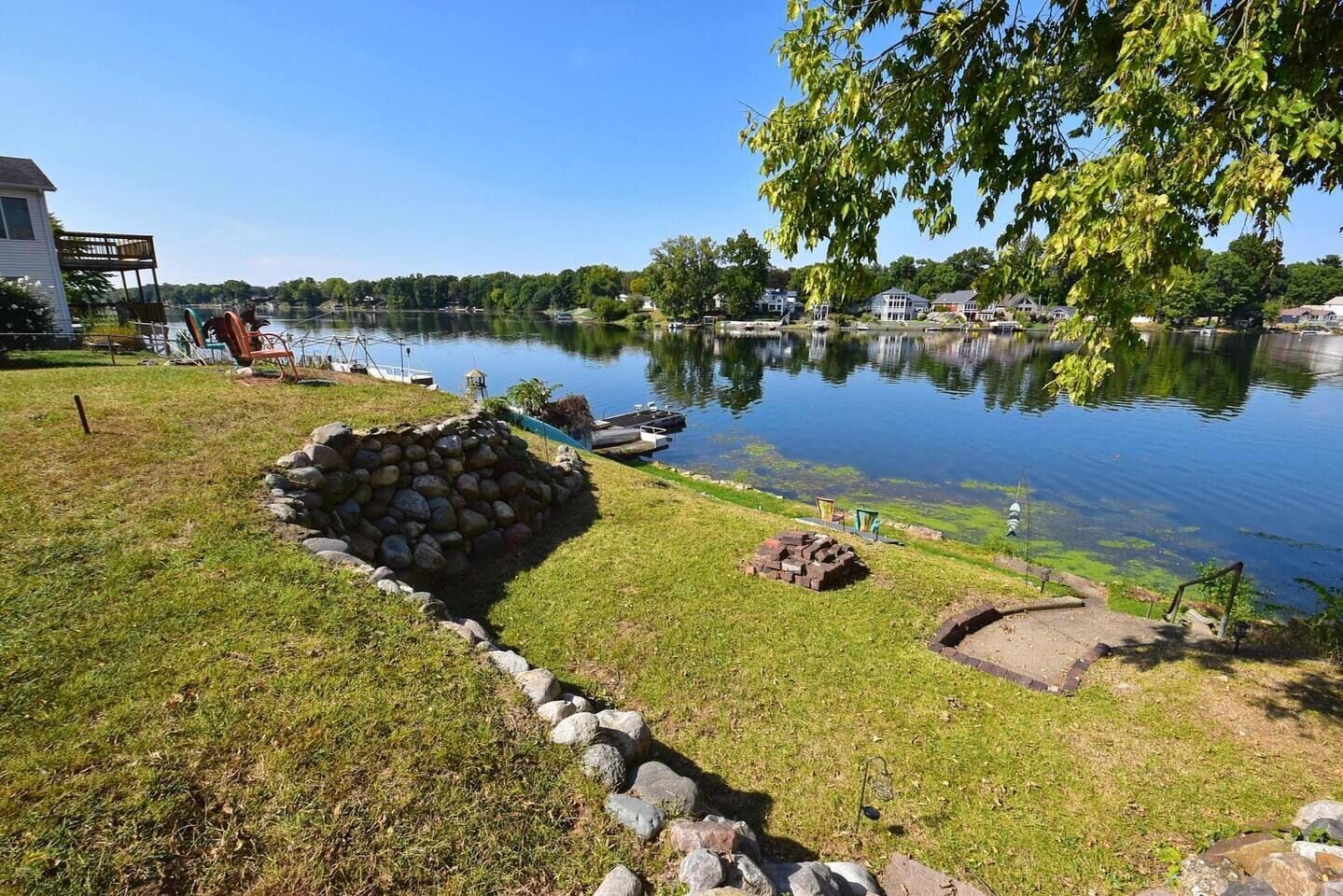 A lakeside property with a stone fire pit, a grassy area, and a dock extending into the water.