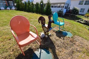 A grassy outdoor area with two chairs, one orange and one blue, and a rusty metal sculpture. - The Chicken Coop, a Modern Riverfront Oasis (908) (Osceola)