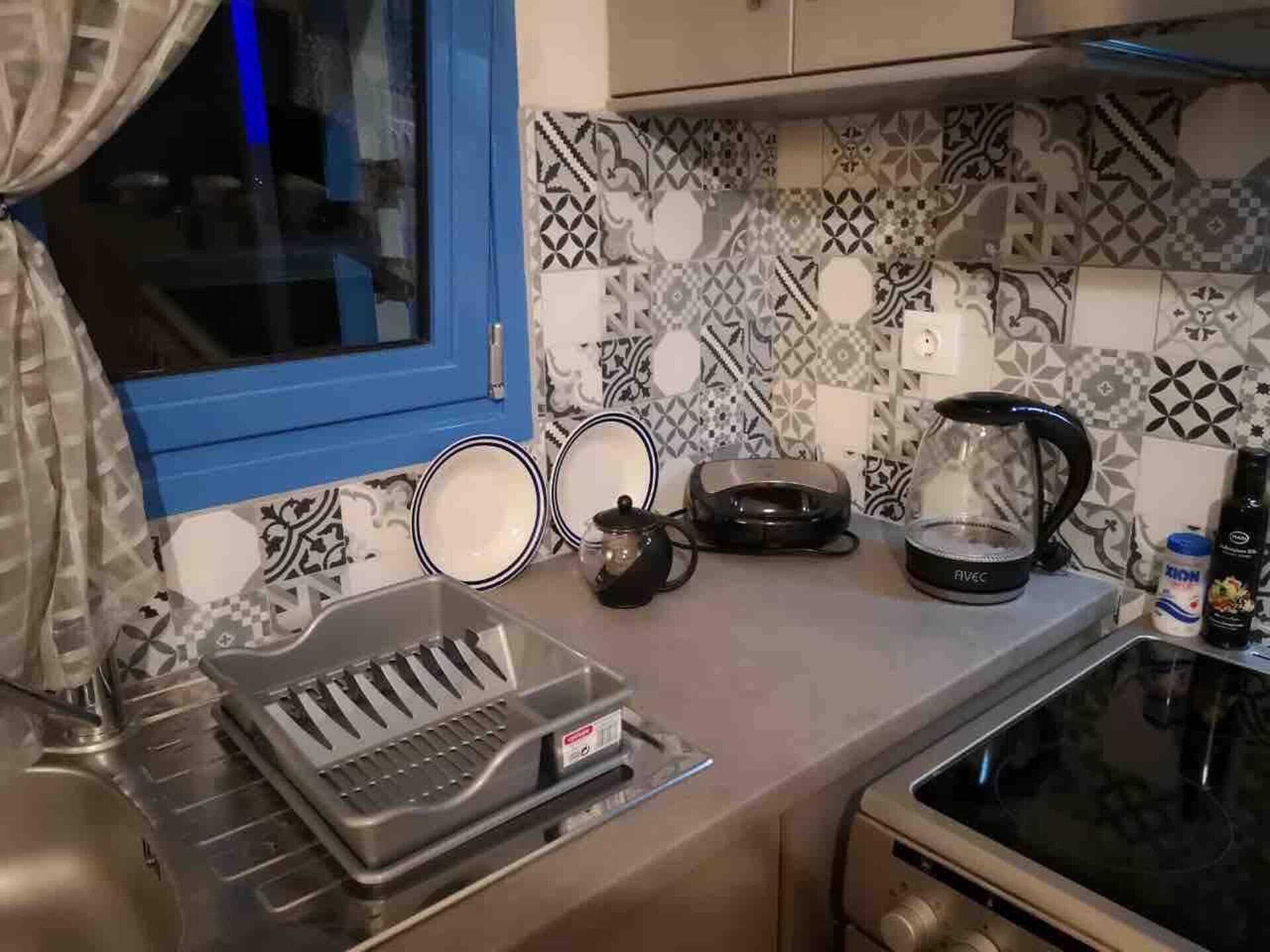 A kitchen with a patterned backsplash, a window with curtains, a coffee maker, and a toaster.