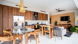 Une cuisine moderne avec des meubles en bois, un îlot central et un coin repas comprenant des chaises et une table en verre.
