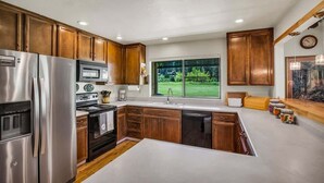 A modern kitchen with wooden cabinets, stainless steel appliances, a large window, and a view of greenery. - Views of the 8th Fairway at Plumas Pines-8 Aspen (Blairsden)