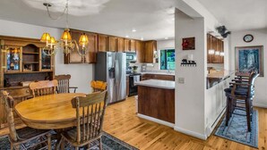 A modern kitchen with wooden cabinets, a central island, and a dining area with a wooden table and chairs. - Views of the 8th Fairway at Plumas Pines-8 Aspen (Blairsden)