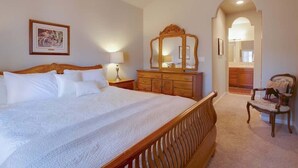 A bedroom with a large bed, a wooden dresser, a mirror, and a chair. - Mountain Oaks - 35 Oak Court PET! (Blairsden)