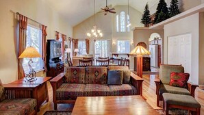 A spacious living room with a large sofa, wooden coffee table, and a dining area with a chandelier. - Mountain Oaks - 35 Oak Court PET! (Blairsden)