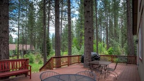 A wooden deck with a round table and chairs, surrounded by tall trees. - Mountain Oaks - 35 Oak Court PET! (Blairsden)