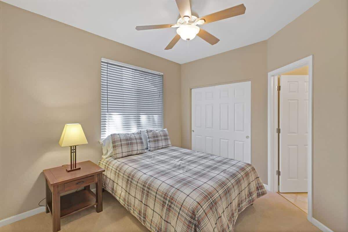 A bedroom with a bed, a nightstand, a ceiling fan, a window with blinds, and a door.