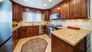A kitchen with wooden cabinets, stainless steel appliances, a granite countertop, and a patterned rug. - Peace on the Pond - 70 Pond (Blairsden)