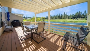 A covered outdoor deck with a table and chairs, overlooking a river and forested area. - Peace on the Pond - 70 Pond (Blairsden)