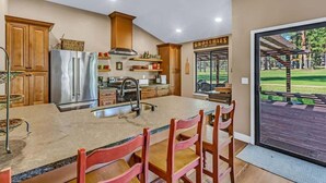 A modern kitchen with a large island, wooden cabinets, stainless steel appliances, and a view of a patio with a pergola. - Stunning on the 17th Fairway - 119 Cottonwood Dr (Blairsden)