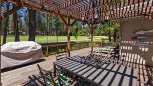Une terrasse en bois avec un espace barbecue couvert, des sièges d’extérieur et une vue sur un terrain de golf.