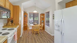 Une cuisine avec des meubles de rangement en bois, un réfrigérateur blanc, une table à manger avec des chaises et un luminaire suspendu.