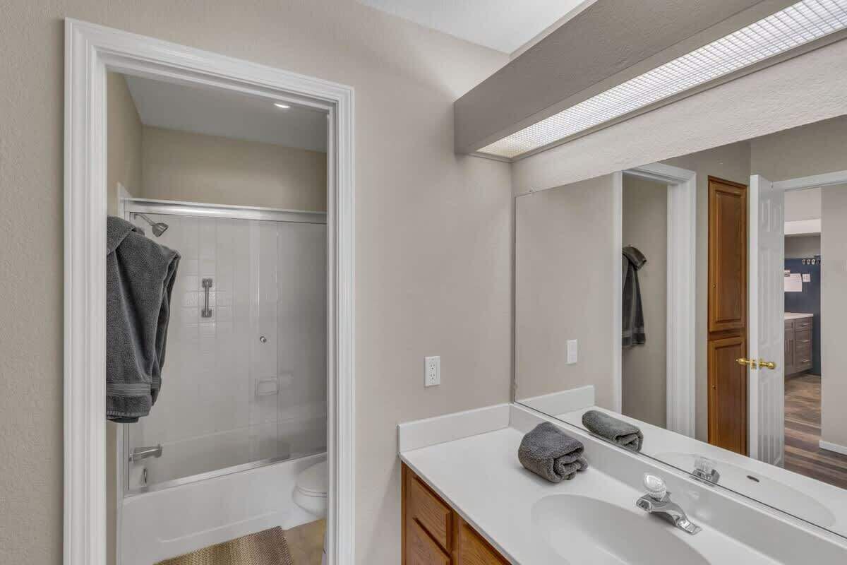 Un baño moderno con cabina de ducha, un espejo grande y un tocador blanco con una toalla.