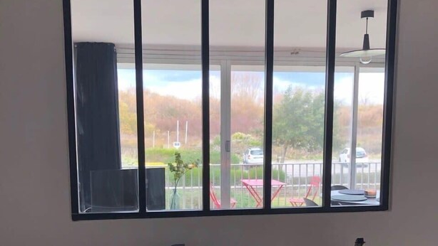 Un dormitorio con un ventanal grande, una cama con almohadas estampadas, una mesita de noche con una lámpara y vistas a un estacionamiento y árboles.