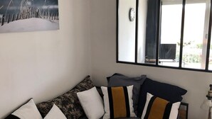 Un salón con sofá, almohadones, un cuadro, un espejo grande y una ventana con vistas.