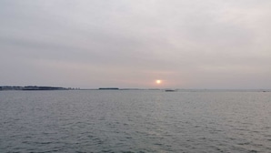 Ein ruhiges Meer, in der Ferne ein untergehende Sonne am Horizont.
