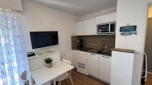 Kompakti keittiö, jossa on litteänäyttöinen televisio, mikroaaltouuni, kahvinkeitin ja jääkaappi.