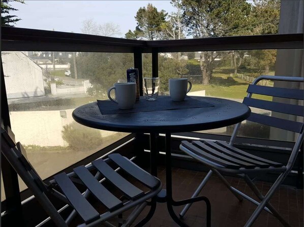 A small round table with two white cups and a glass on a balcony with metal chairs.