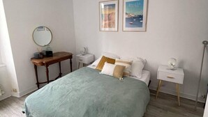 Een slaapkamer met een bed, nachtkastjes, een spiegel en twee prenten in een lijst aan de muur.