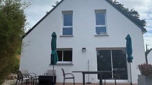 A two-story house with a white exterior, a wooden deck, and two green umbrellas. - Maison Tamaris. avec jardin et clos (Quiberon)
