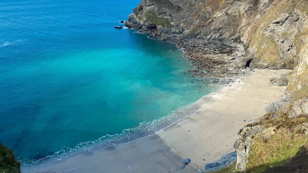 Un paysage côtier avec une plage, des falaises et une eau d’un bleu limpide.