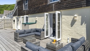 Une terrasse en bois aménagée avec du mobilier d’extérieur, notamment des canapés et des tables.