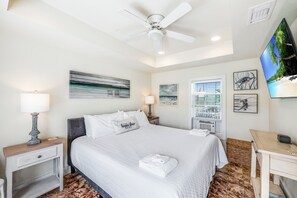 Une chambre d’hôtel comprenant un lit, deux tables de chevet avec des lampes, un ventilateur de plafond, une télévision et des œuvres d’art accrochées aux murs.