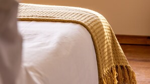 Une chambre à coucher avec un lit, une fenêtre donnant sur des arbres et une étagère avec des livres et une bouteille.