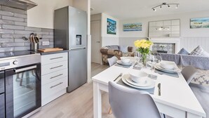 Une cuisine moderne équipée d’un four encastré, d’un réfrigérateur et d’un coin repas avec une table dressée pour quatre personnes.