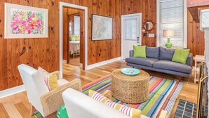 A cozy living room with wooden walls, a sofa, a coffee table, and a ceiling fan. - Caretta Cottage | Steps From the Beach! (Tybee Island)
