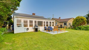Ein Haus mit überdachter Terrasse, Sitzgelegenheiten im Freien und einem Rasen.