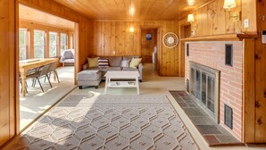 Un accogliente interno di una baita con camino, pareti in legno, un divano e un'area pranzo.