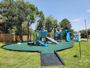 Een speeltuin met glijbanen en klimconstructies, omringd door een hek en bomen.