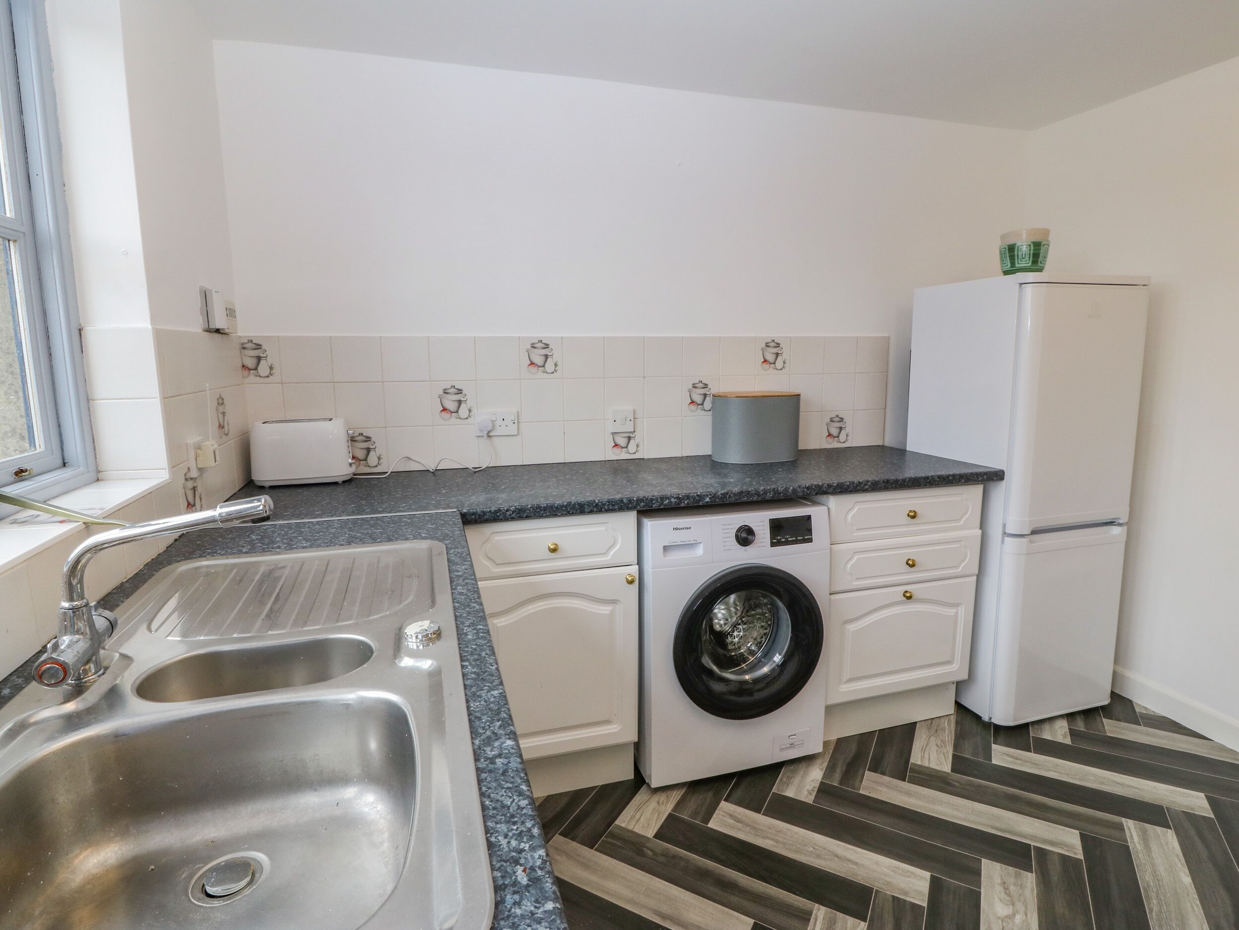 A kitchen with a double sink, a washing machine, a refrigerator, and a window.