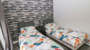 Une petite chambre moderne avec deux lits simples, une tête de lit grise et un mur décoré d’un motif imitant la pierre.