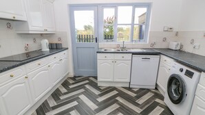 Une cuisine moderne avec des meubles blancs, un sol à motifs en chevrons, un lave-linge et une fenêtre donnant sur un espace verdoyant.