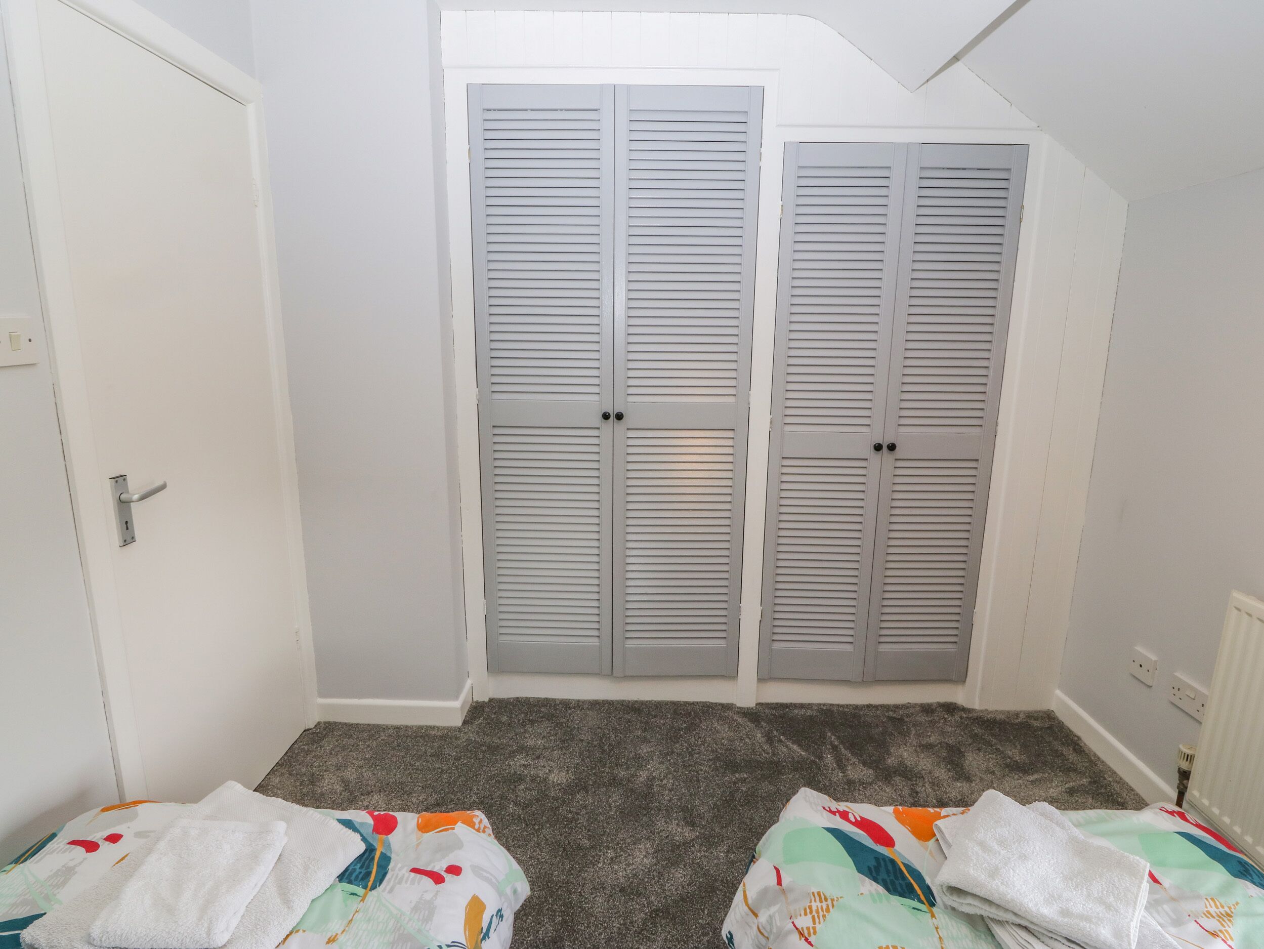 A room with a white door, grey louvered closet doors, and a carpeted floor.