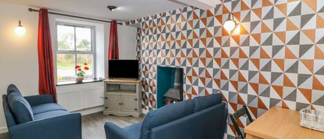 A modern living room with a TV, blue sofas, a wooden table, and a patterned wall.