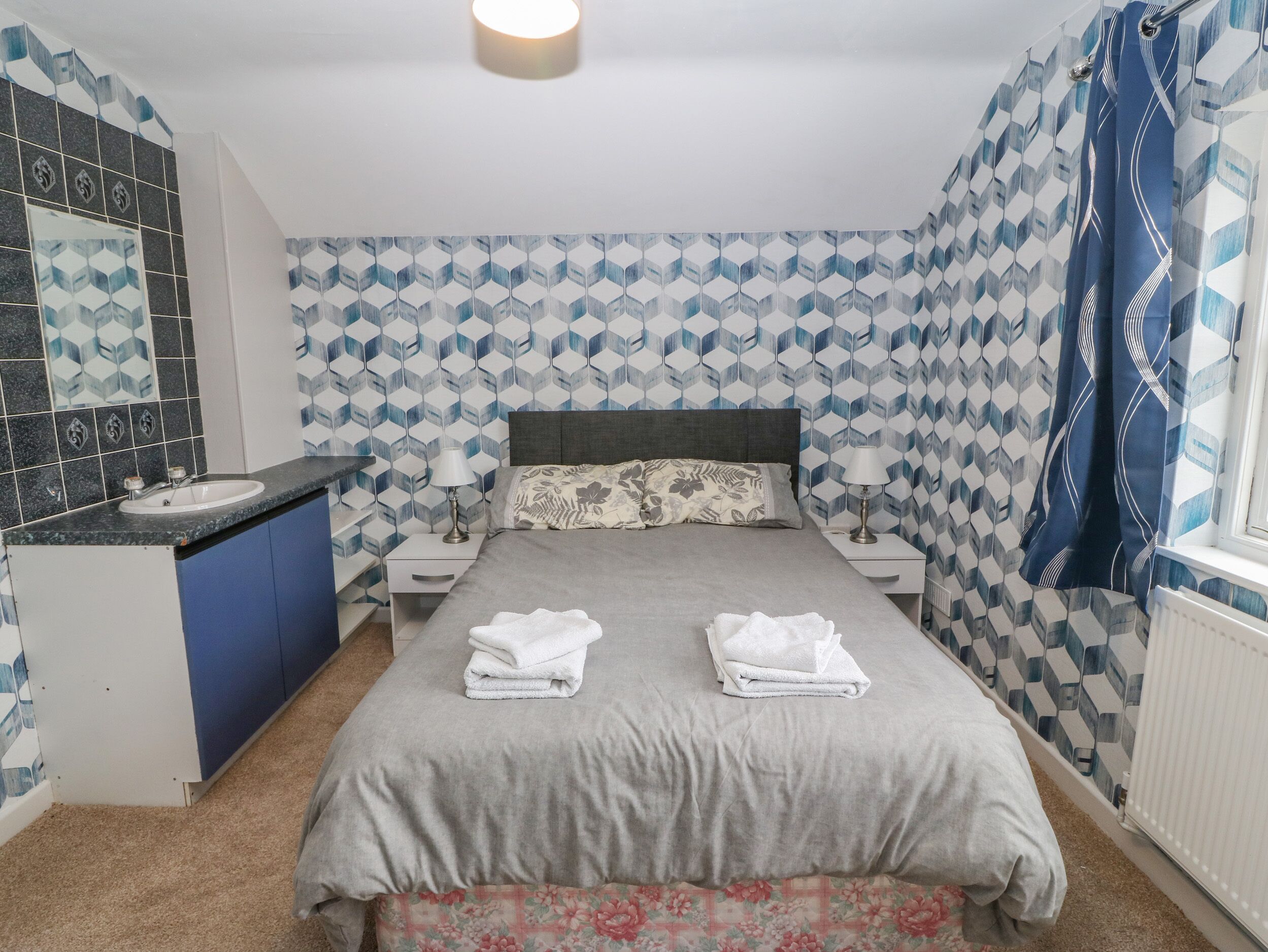A bedroom with a bed, nightstands, a sink, and a mirror.