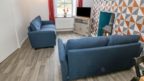 Un salon moderne avec deux canapés bleus, un téléviseur posé sur un meuble en bois, une cheminée et un mur orné d’un motif géométrique.