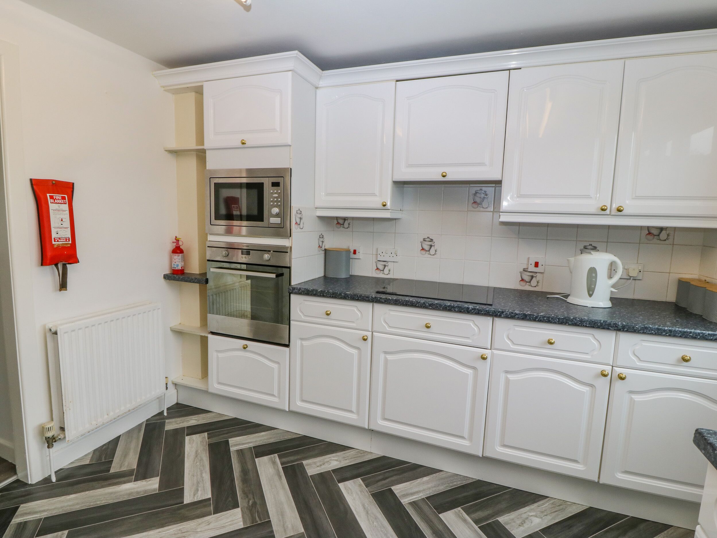 A kitchen with white cabinets, a microwave, an oven, and a kettle on the countertop.