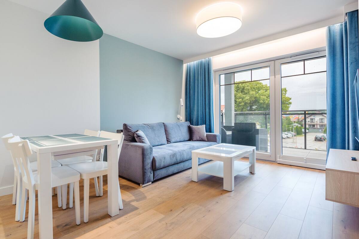 A modern living room with a dining table, white chairs, a grey sofa, and a small white table.