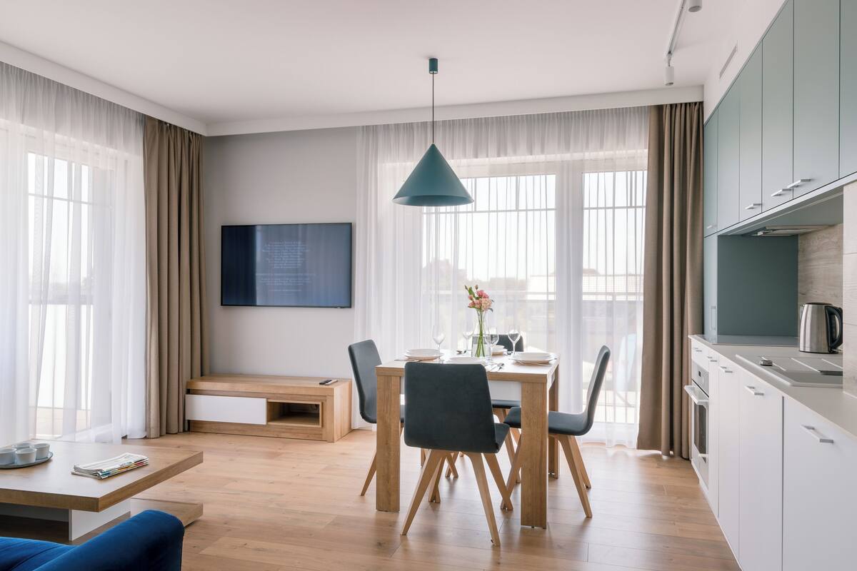 A modern living room with a dining table, chairs, a sofa, a TV, and a kitchen area.
