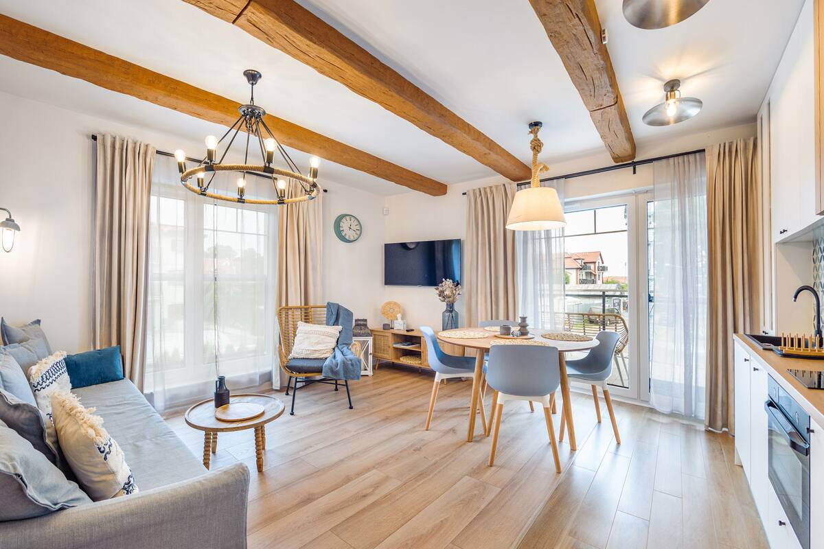 A spacious living area with a wooden ceiling, a dining table with chairs, a sofa, and a television.