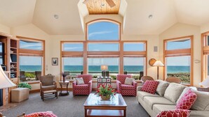 A spacious living room with large windows, a high ceiling, and a view of the ocean. - Dutch Treat: Oceanfront | Private Pool | Elevator (Corolla)