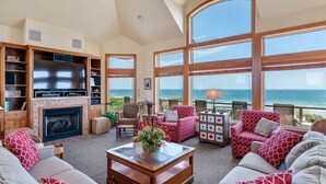 A spacious living room with a fireplace, large windows overlooking the sea, and comfortable seating. - Dutch Treat: Oceanfront | Private Pool | Elevator (Corolla)