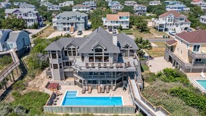 A large, multi-story house with a prominent front deck, a swimming pool, and a dock. - Dutch Treat: Oceanfront | Private Pool | Elevator (Corolla)