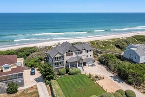 A coastal residential area with a large house featuring a covered patio, a driveway, and a view of the beach. - Dutch Treat: Oceanfront | Private Pool | Elevator (Corolla)
