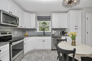 A kitchen with white cabinets, a microwave, a stove, a sink, and a dining area with a table and chairs.